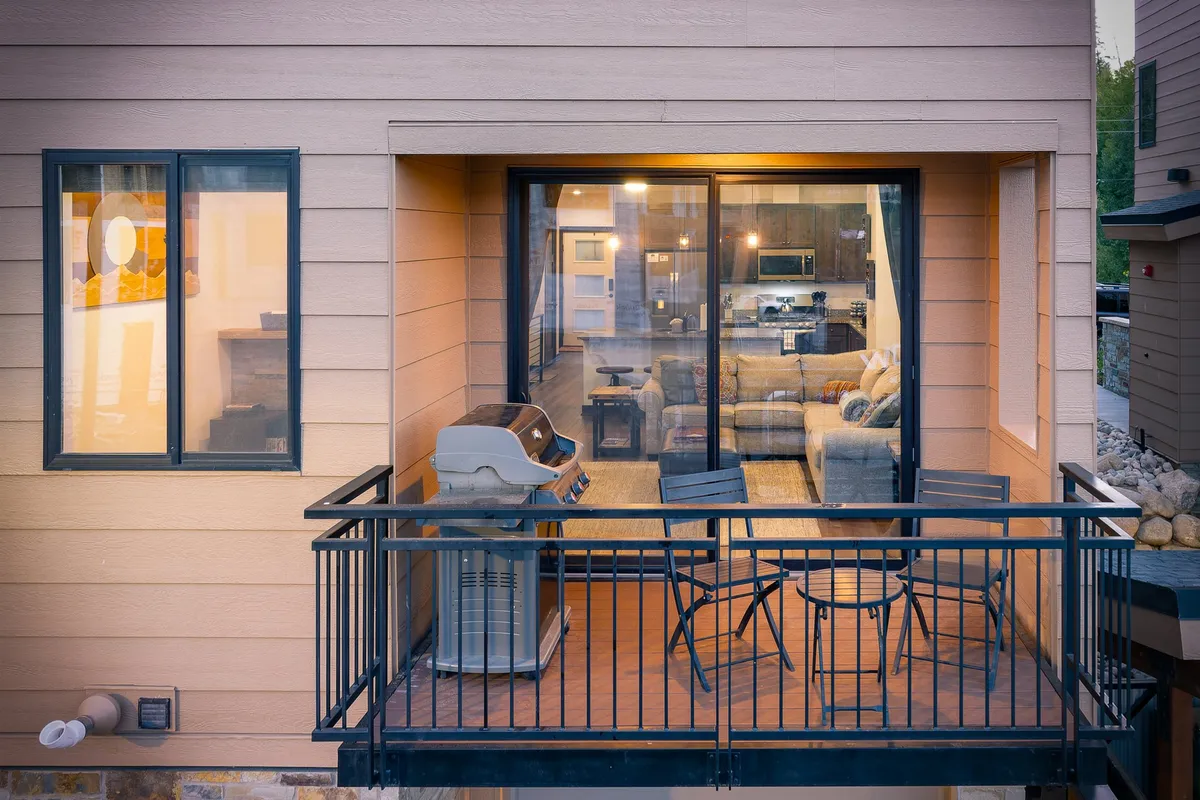 A balcony with seating and a grill overlooks the living room, offering sunset views and an inviting space for outdoor dining or intimate conversations. The image bridges the interior and exterior, emphasizing the ease of accessing fresh air and beautiful mountain surroundings.