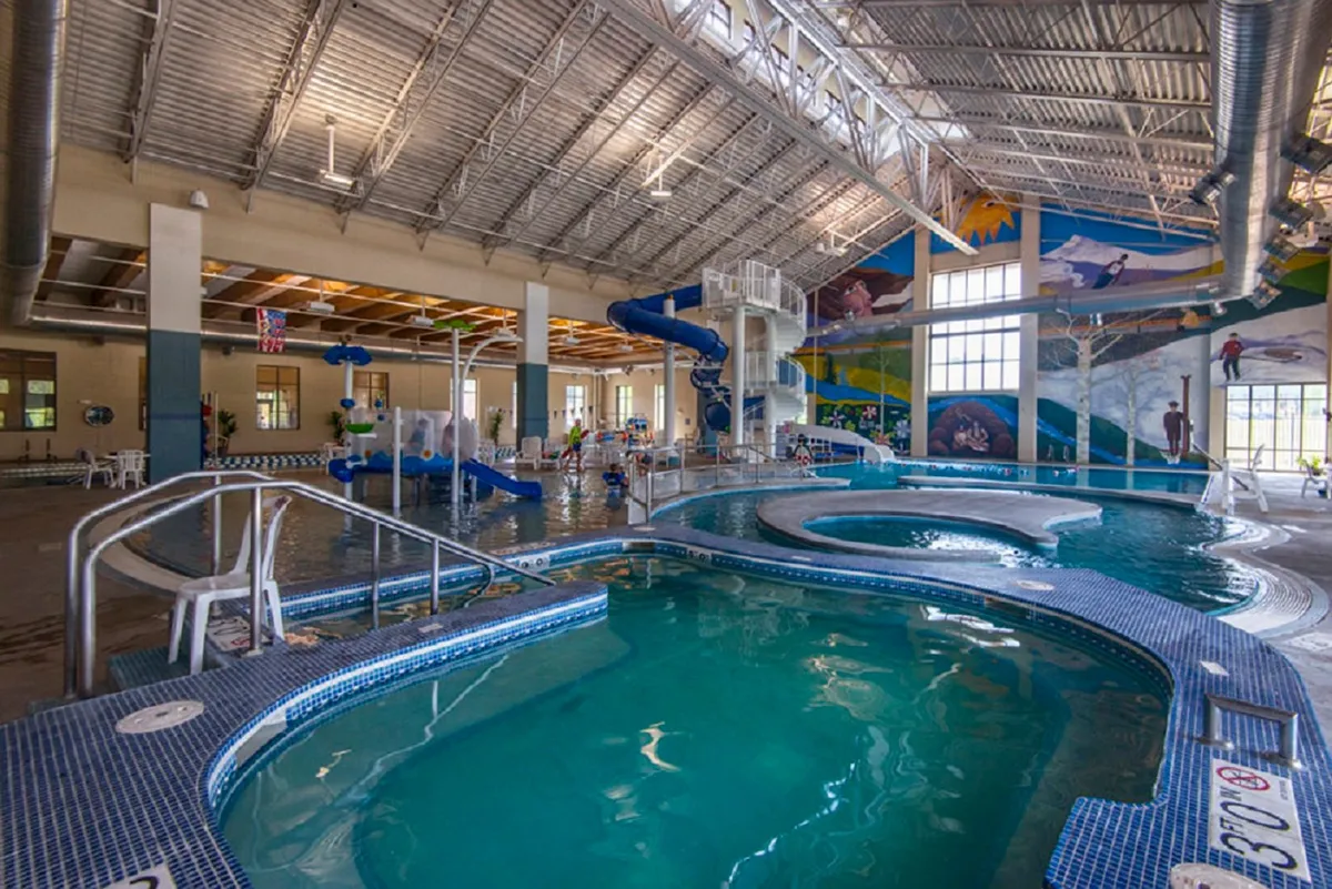 A vibrant indoor recreation area featuring colorful swimming pools, playful water slides, and children having fun. The lively murals and energetic atmosphere evoke the amenities often found at luxury resorts.