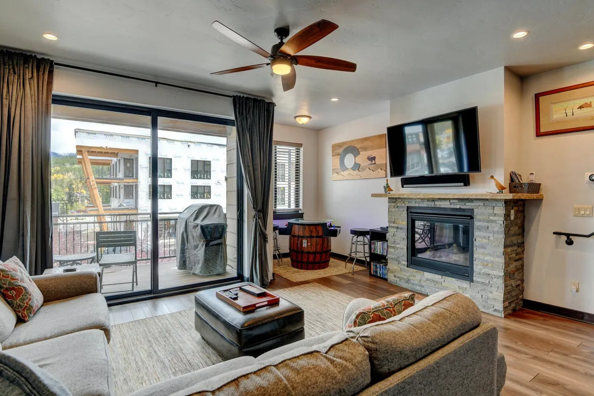 A cozy living room featuring a modern fireplace, plush sofa, and large balcony doors that open to scenic mountain views. The setup encourages relaxation while also providing a visual connection to the outdoors, hinting at the adventure waiting just beyond the home.
