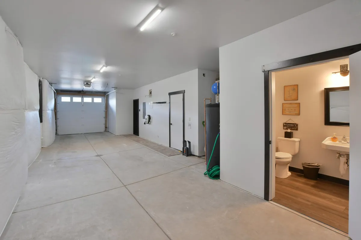 A spacious garage interior with a prominent garage door, utility hooks along the wall for gear storage, a sink for quick cleanup, and an adjacent bathroom entrance. The area is clean and functional, ideal for storing vehicles, outdoor equipment, and preparing for adventure outings.