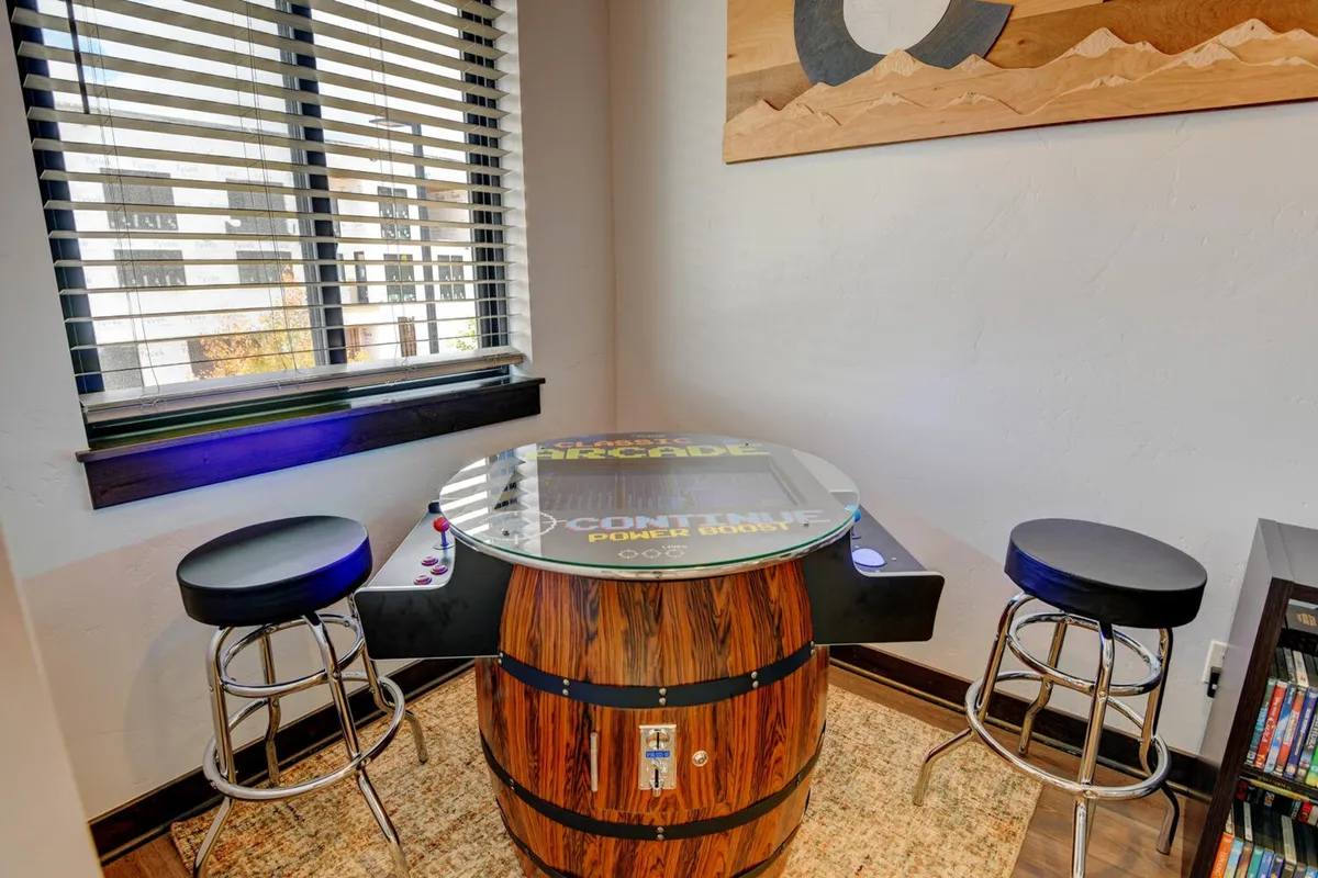 A fun arcade area with a classic arcade-style table featuring a barrel base and stools. The setup invites guests to enjoy nostalgic video games and social interaction in a dedicated space for play.