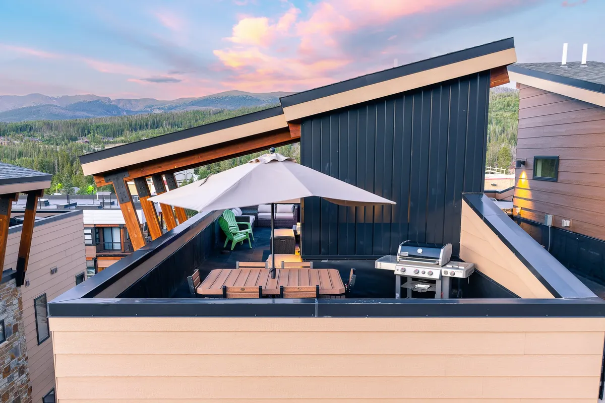 This exterior shot features an outdoor dining area with a grill, a patio umbrella, and comfortable seating. The mountain view in the background sets the stage for relaxed outdoor gatherings, while the setup suggests both casual barbecues and sophisticated sunset cocktails.