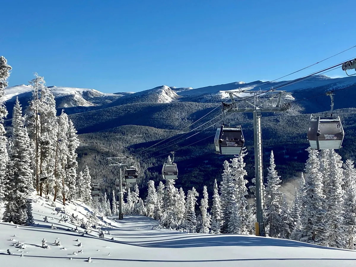 An exterior scene of a ski lift ascending snow-covered mountains surrounded by pine trees. The sky is clear, and the area appears serene yet full of promise for adventurous activities such as skiing, snowboarding, and snowshoeing.
