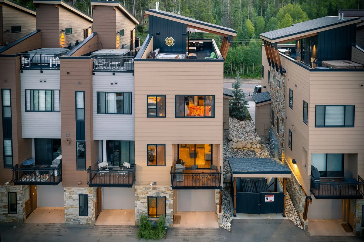 The image shows the exterior of the building with distinctive balconies, large windows, and a unique roof design. It hints at the rooftop deck’s location and provides context for the elevated, private position of this premium end unit. There is a welcoming mood, with space for outdoor lounging and gatherings.