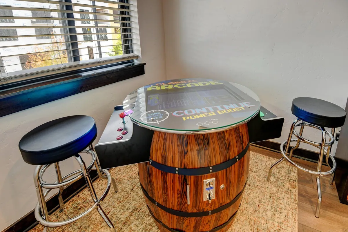 A dedicated arcade area with a classic arcade game table, barrel-style base, and stools, offering a fun and nostalgic environment for socializing and gaming.