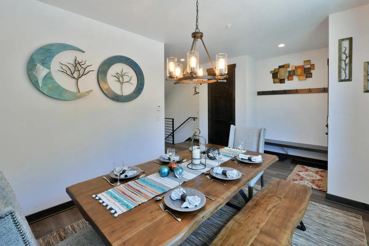A warm, inviting dining area featuring a large wooden table, decorative wall art, and a stylish light fixture. The table is set for a group, highlighting the potential for family dinners, festive celebrations, or game nights. The atmosphere is cozy and welcoming.