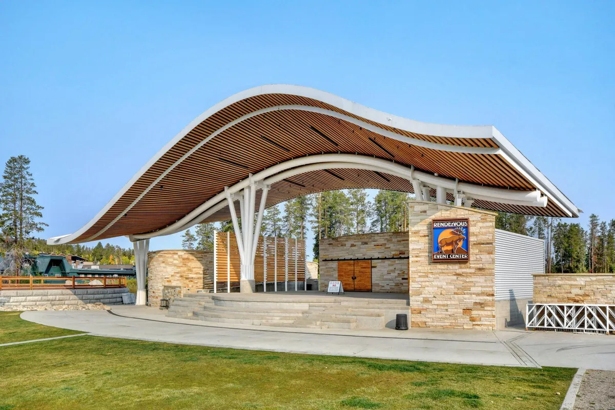 An exterior view of Hideaway Park's amphitheater, featuring a modern curved roof structure, stone façade, and an open stage area ready for outdoor concerts or community gatherings. The setting is open, welcoming, and designed for memorable public events.