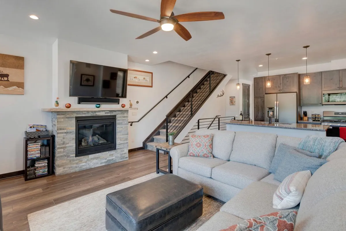 A spacious open-concept living area with a plush sofa, modern fireplace, and a bright kitchen island in view. The room is filled with natural light from panoramic windows, creating an airy atmosphere perfect for gatherings. The fireplace anchors the space, while the kitchen island invites casual conversations and family brunches.
