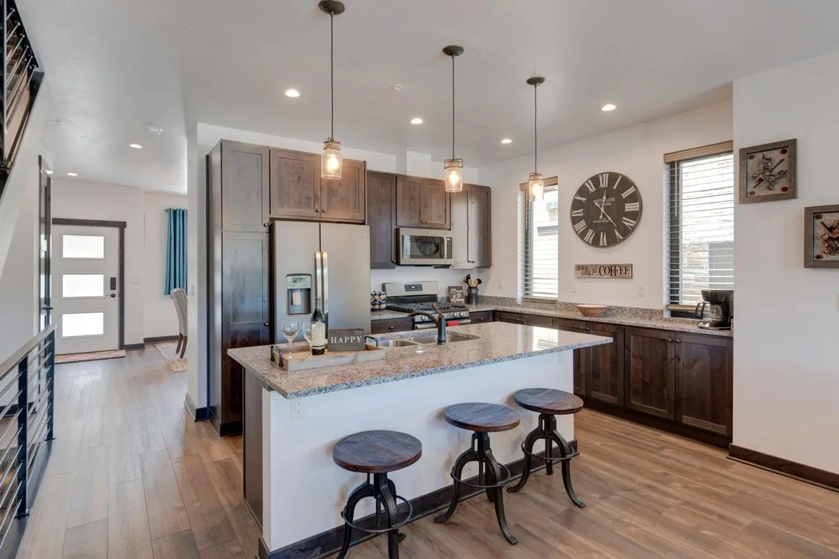 A chef-inspired kitchen with granite countertops, modern stainless steel appliances, and wooden stools at the counter. The space looks both functional and welcoming, ideal for meal prep, coffee mornings, or casual conversations while cooking.